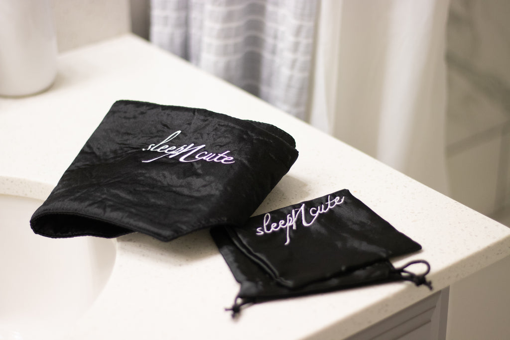 Black Sleep N Cute satin headwrap and matching storage pouch displayed on a bedside table