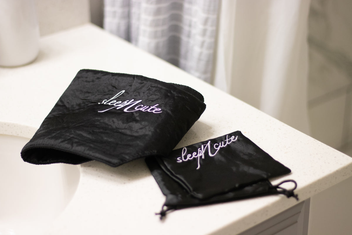 Black Sleep N Cute satin headwrap and matching storage pouch displayed on a bedside table